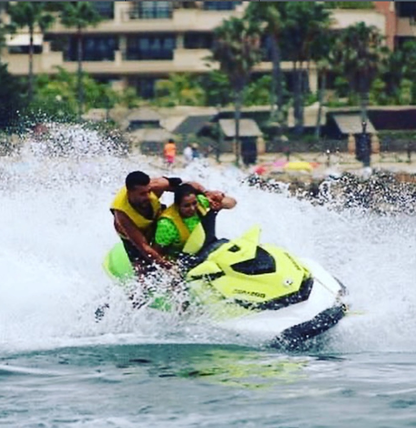 Two riders on a yellow Sea-Doo jet ski cutting through the surf