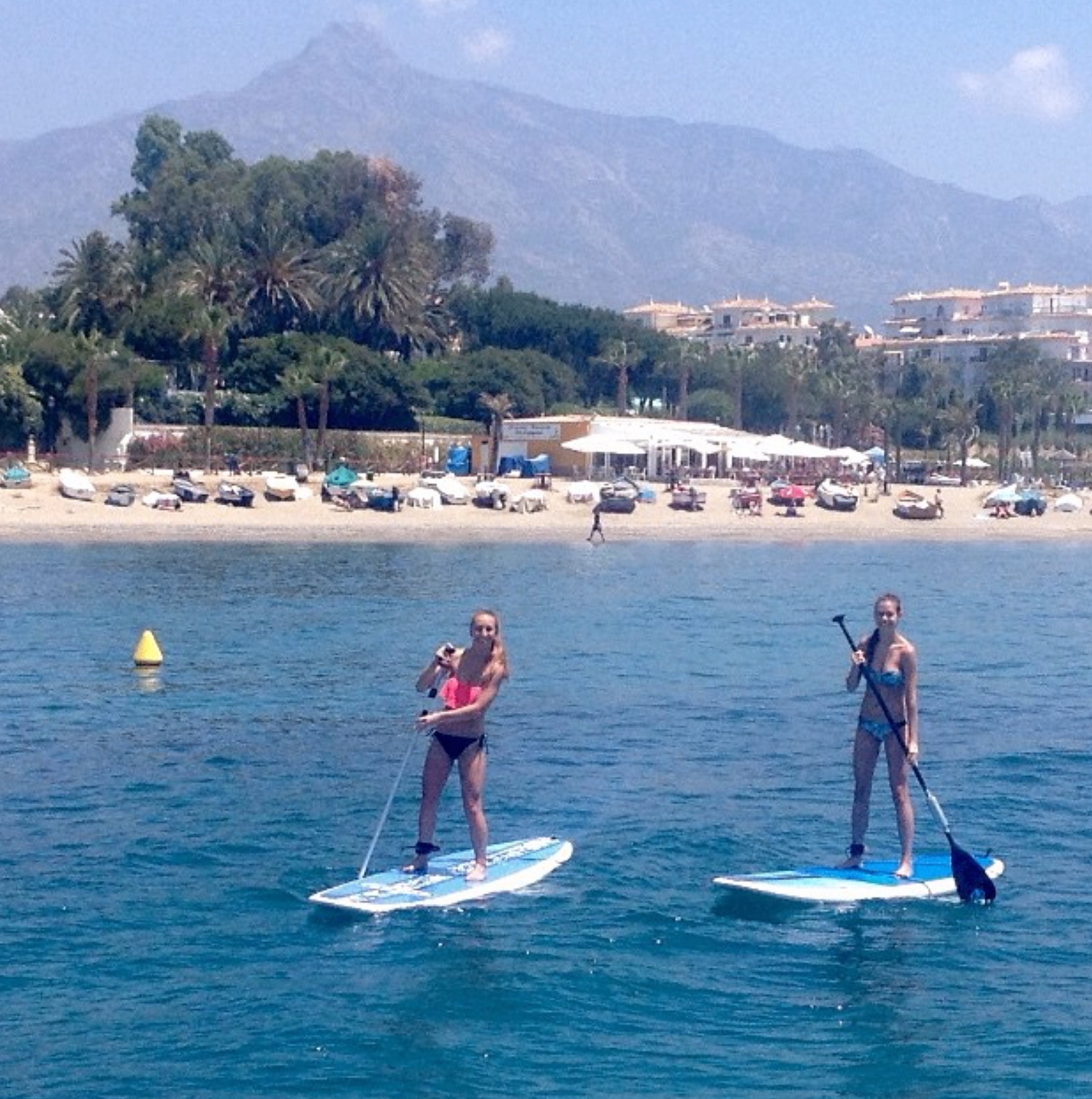 Two paddle boarders gliding across the bay with Marbella mountain views